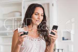 Pretty brunette using smartphone and having glass of wine