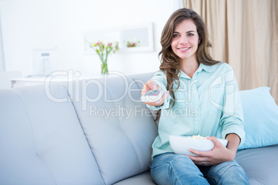 Happy brunette watching television with bowl of popcorn