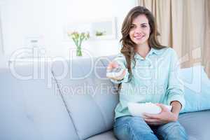 Happy brunette watching television with bowl of popcorn