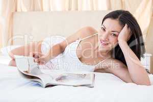 Pretty brunette reading a magazine on bed
