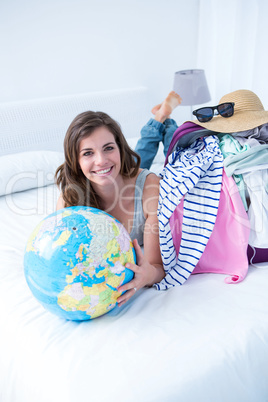 Smiling brunette lying on bed holding her globe