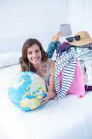 Smiling brunette lying on bed holding her globe