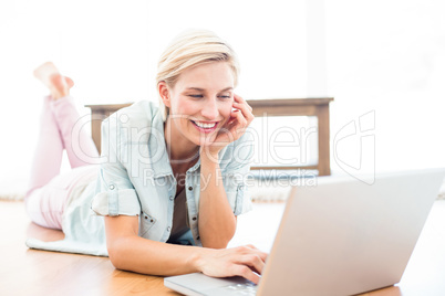 Pretty blonde woman lying on the floor and using her laptop