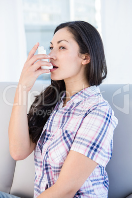 Pretty brunette using inhaler on couch