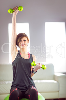 Fit woman lifting dumbbell sitting on ball