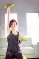 Fit woman lifting dumbbell sitting on ball