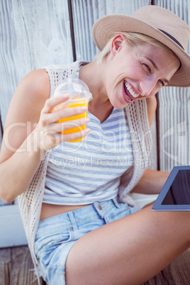 Pretty blonde woman using her tablet and holding orange juice