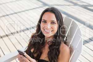 Pretty brunette sitting on a chair and texting with her mobile p