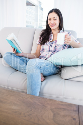 Pretty brunette looking at camera and holding a book and a mug o
