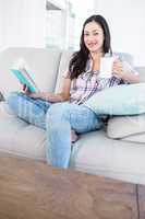 Pretty brunette looking at camera and holding a book and a mug o