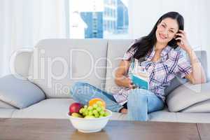 Pretty brunette looking at camera and reading a book on couch
