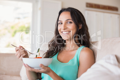 Pretty brunette eating salad on couch