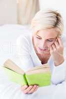 Smiling blonde woman lying on the bed and reading a book