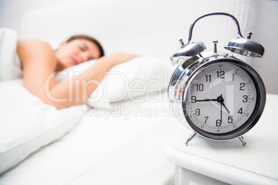 Pretty brunette sleeping in bed with alarm clock