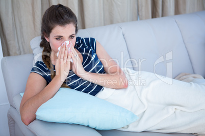 Sick woman blowing her nose on couch