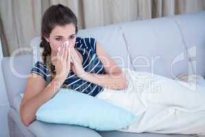 Sick woman blowing her nose on couch