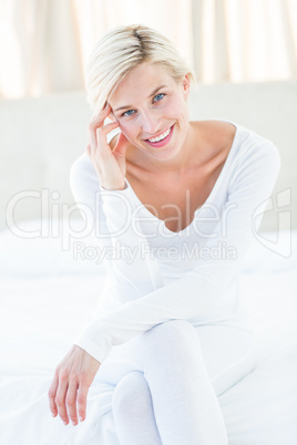 Pretty blonde woman smiling at the camera while sitting on the b
