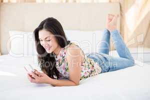 Pretty brunette using smartphone on bed