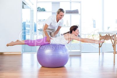 Trainer helping woman on exercise ball
