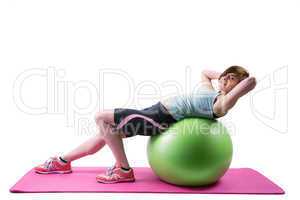 Pretty brunette looking at camera and exercising on fitness ball