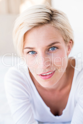 Smiling blonde woman lying on the bed and looking at camera