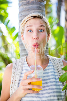 Pretty blonde woman smiling at the camera and drinking orange ju
