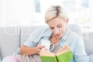 Pretty blonde woman reading a book and holding a mug
