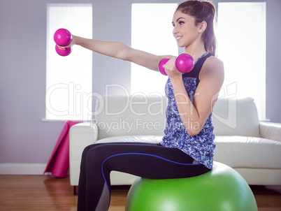 Fit woman lifting dumbbells on exercise ball