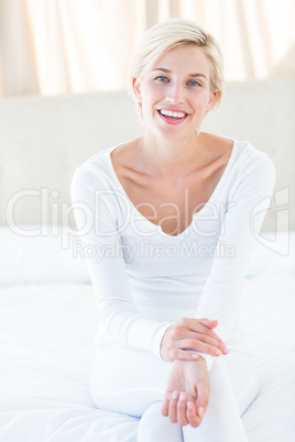 Pretty blonde woman smiling at the camera while sitting on the b