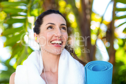 Fit beautiful brunette listening music and holding exercise mat