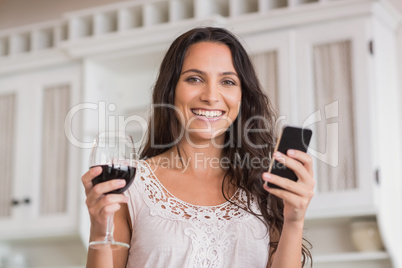 Pretty brunette using smartphone and having glass of wine