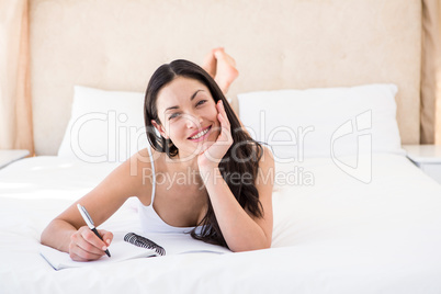 Pretty brunette looking at camera and writing on bed