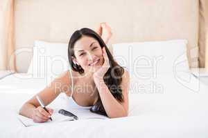 Pretty brunette looking at camera and writing on bed