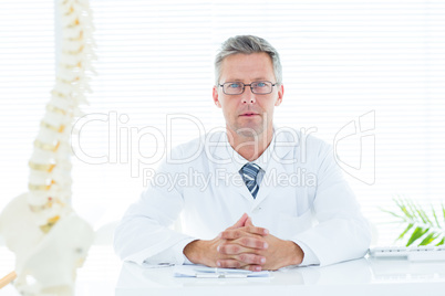 Doctor sitting at his desk looking at camera