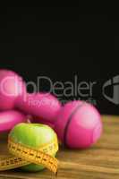Pink dumbbells with green apple and measuring tape