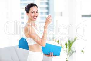 Brunette holding glass of water and exercise mat