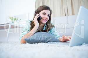 Happy brunette on the phone using her laptop