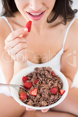 Pretty brunette eating strawberries on bed