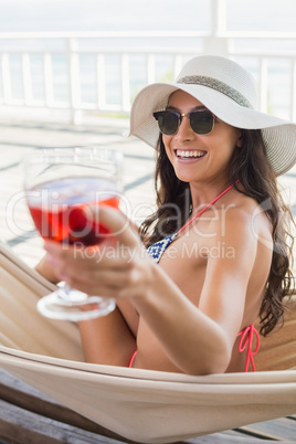 Pretty brunette relaxing on a hammock and drinking cocktail