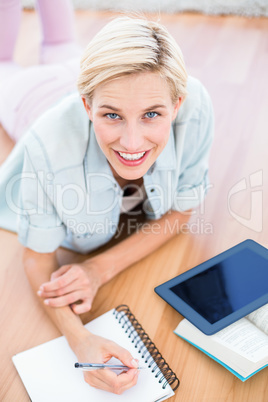 Pretty blonde woman lying on the floor and taking notes while us