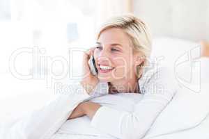 Smiling blonde woman lying on the bed and calling on the phone