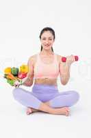 Fit brunette lifting dumbbell and holding bowl of salad