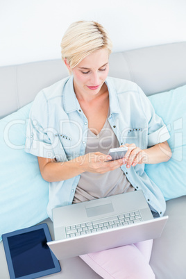 Pretty blonde woman using her laptop and texting with her mobile