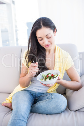 Pretty brunette eating salad on couch