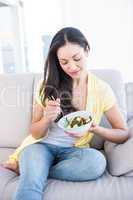 Pretty brunette eating salad on couch