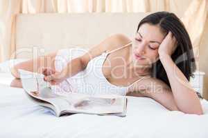 Pretty brunette reading a magazine on bed