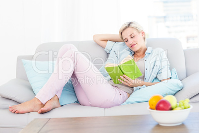 Pretty blonde woman reading a book on the couch