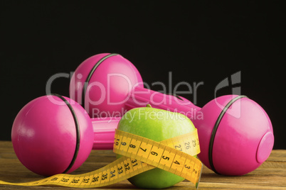 Pink dumbbells with green apple and measuring tape