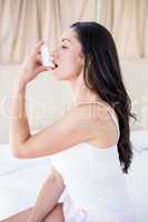 Pretty brunette using inhaler on bed