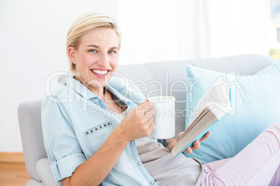 Pretty blonde woman reading a book and holding a mug